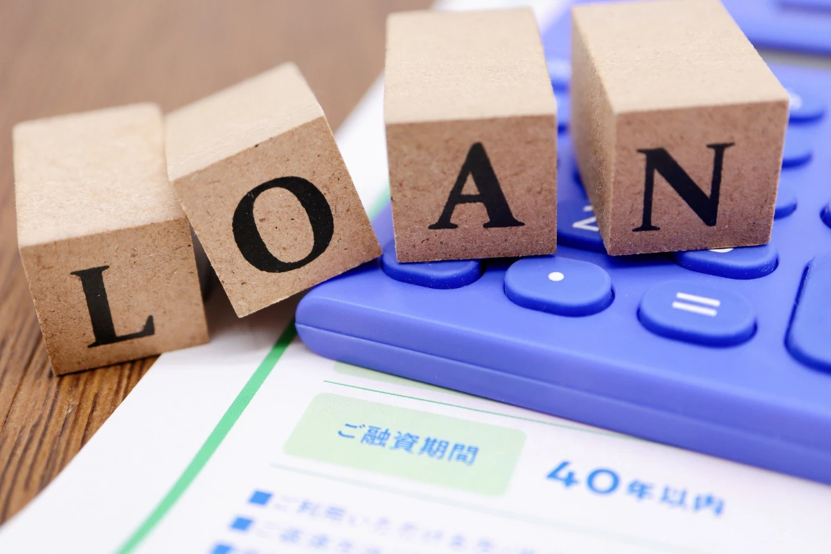 Loan letters on wooden blocks with blue loan calculator and repayment document on wooden desk.